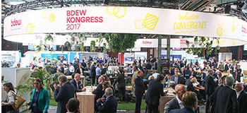 Belebte Ausstellungshalle auf dem BDEW-Kongress 2017 mit Menschen, die sich unter einem groÃŸen runden Banner an Tischen und StÃ¤nden vernetzen.