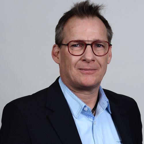 Professionelles PortrÃ¤tfoto einer Person, die eine dunkle Anzugjacke Ã¼ber einem hellblauen Hemd mit Kragen trÃ¤gt, verwendet fÃ¼r ITVT-Unternehmensmaterialien.