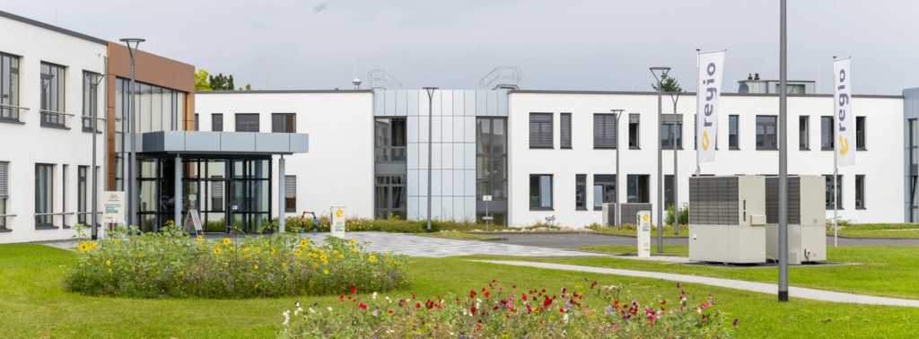 Modernes weiÃŸes BÃ¼rogebÃ¤ude mit Glaseingang, Landschaftsgarten und AuÃŸenausstattung.
