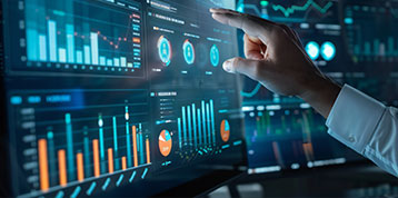 Eine Person, die auf einen Computerbildschirm zeigt, auf dem verschiedene Daten und Statistiken angezeigt werden.
