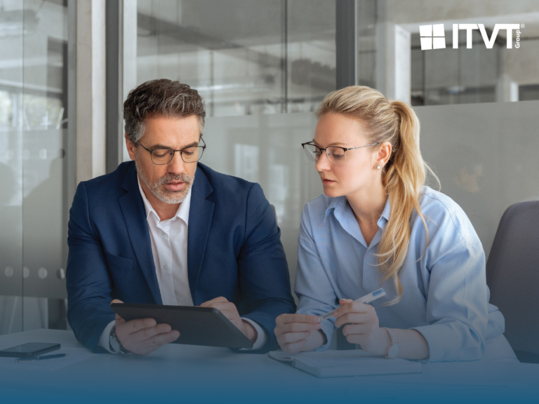 Zwei GeschÃ¤ftsleute, ein Mann in einem blauen Anzug und eine Frau in einem hellblauen Hemd, beide mit Brille, Ã¼berprÃ¼fen Informationen auf einem Tablet in einer BÃ¼roumgebung. Das Logo der ITVT Group ist in der oberen rechten Ecke zu sehen.